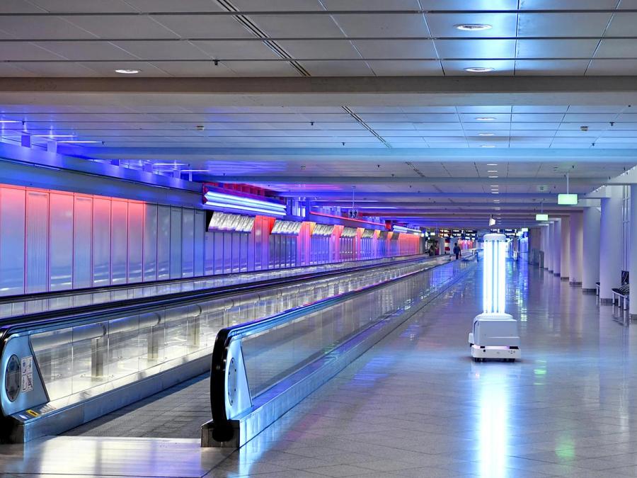 A mobile robot with bright UV lights moves through an empty airport next to a walkway.