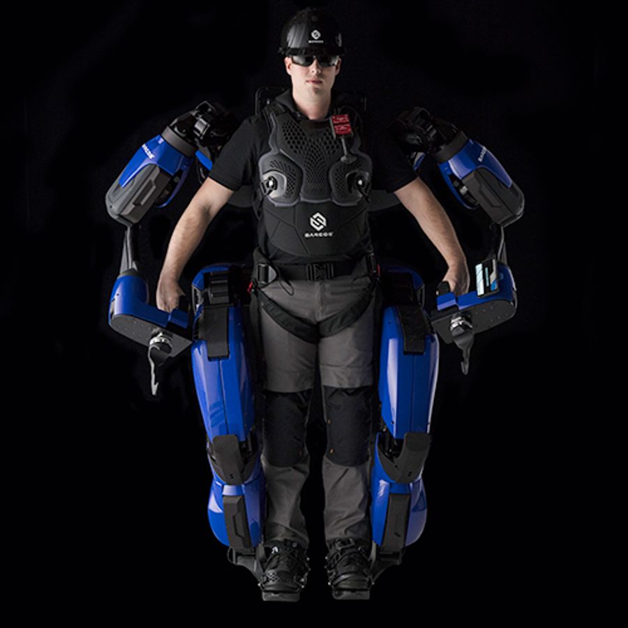 A person in safety helmet, glasses and vest wears a large black and blue full body exoskeleton suit.