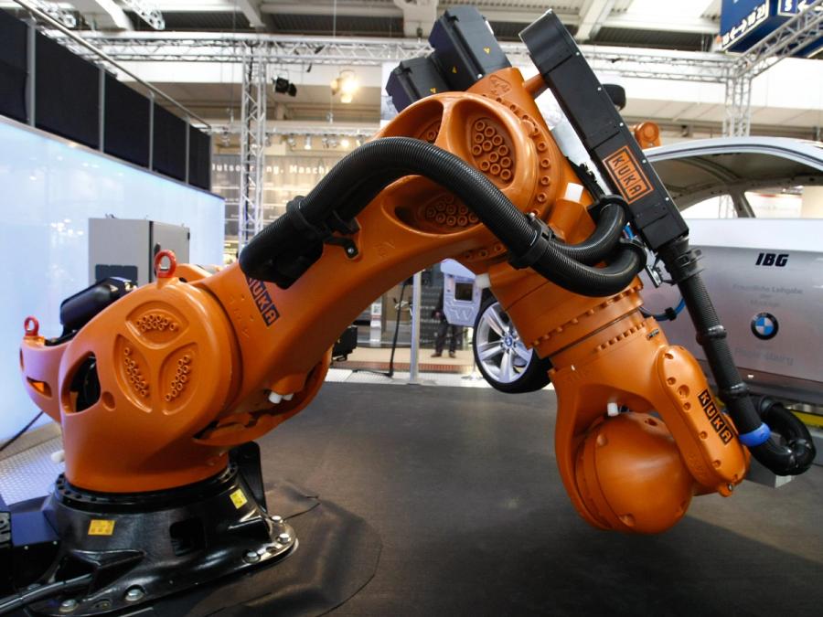 A black base holds a tremendously large orange industrial arm, which is seen picking up a Silver BMW car.