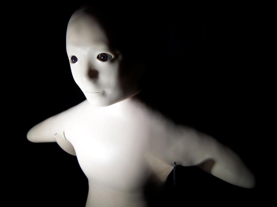 Close-up of Telenoid, a humanoid robot the size of small child, with a soft torso with a bald head, a doll-like face, and stumps in place of limbs.